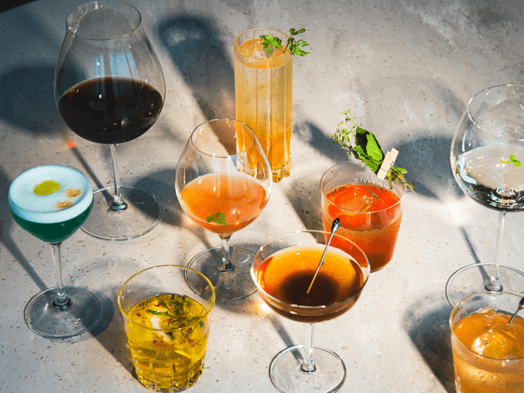 Colorful assortment of cocktails around the world in different glasses with citrus, herbs, and other fresh garnishes.