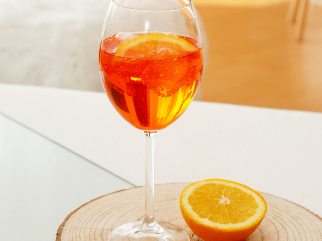 Bright orange spritz cocktail served over ice in a wine glass with a fresh orange slice.