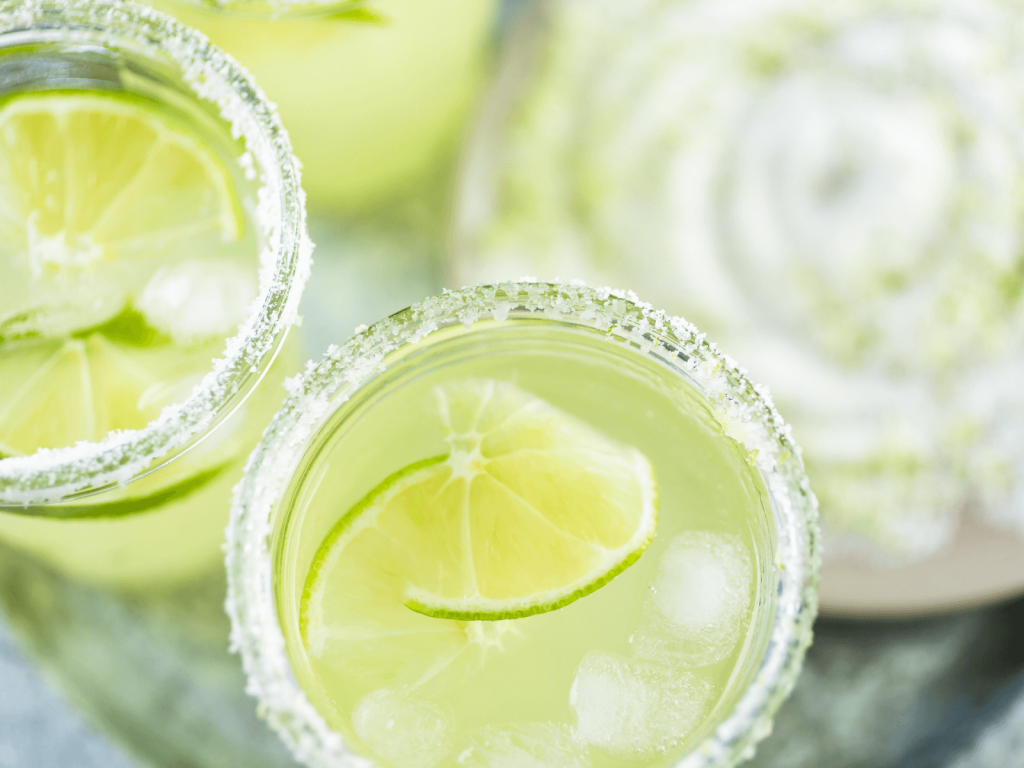Top down view of two pale green margaritas with salted rims, lime slices, and ice, a bright citrus cocktail often featured in cocktails around the world.