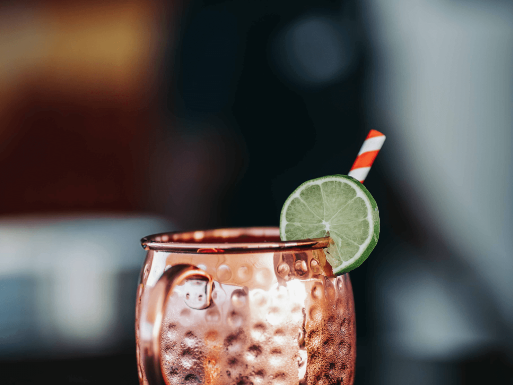 Moscow mule served in a hammered copper mug with a lime wheel and striped straw.