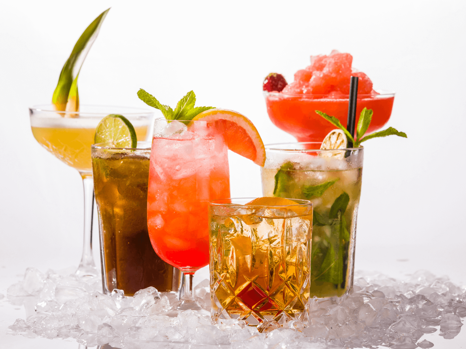 Assorted cocktails around the world displayed on crushed ice, including a mint mojito, a bright pink spritz with grapefruit garnish, a whiskey drink in a cut glass, a dark highball with lime, and a red frozen cocktail in a coupe.