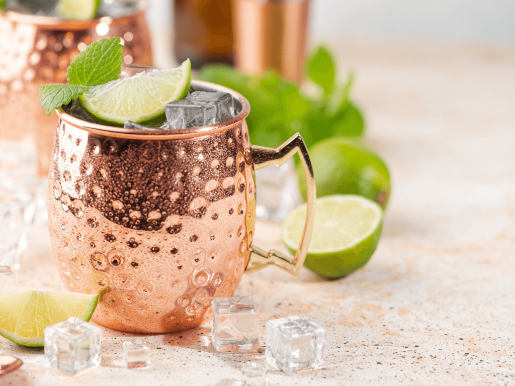 Copper Moscow mule mug filled with ice, topped with a lime wedge and mint, with lime halves and ice cubes on the counter, a popular pick from cocktails from around the world.