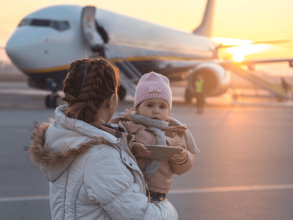 Mother holding a baby near an airplane on the runway at sunset before boarding a flight.