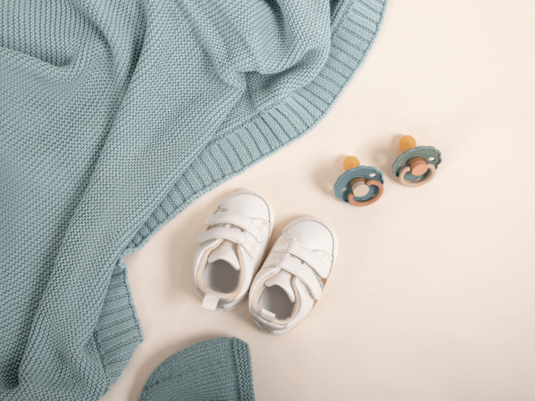 Baby shoes and pacifiers beside a soft blue knitted blanket for flying with a baby.