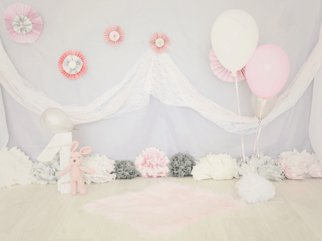 Pink and white first birthday party setup with balloons, paper decorations, a stuffed bunny, and a soft rug, perfect for 1st birthday wishes.