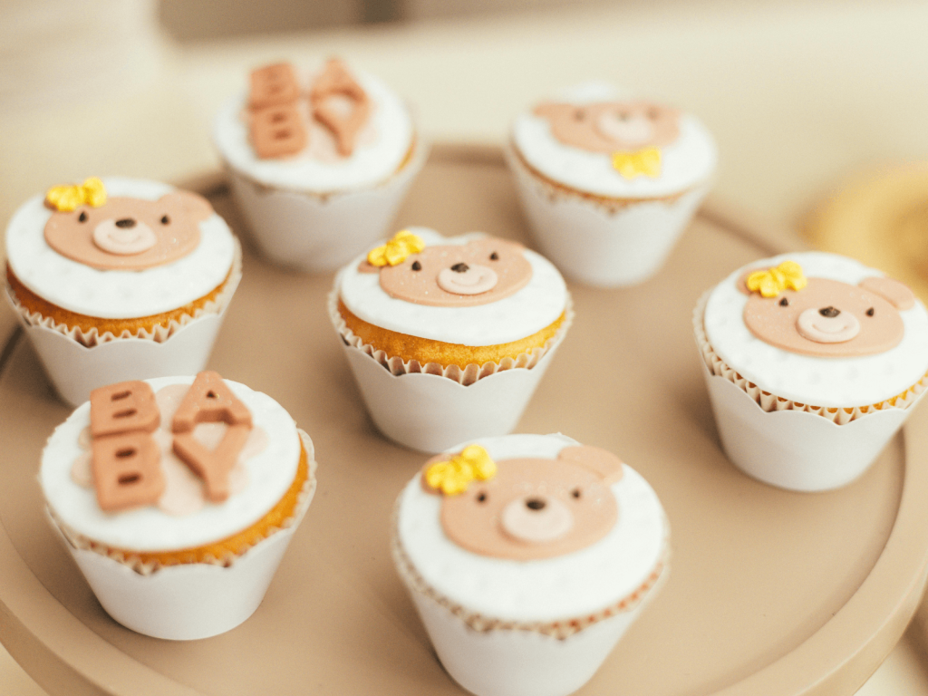 Cupcakes decorated with cute teddy bear faces and baby themed fondant designs for a first birthday celebration.