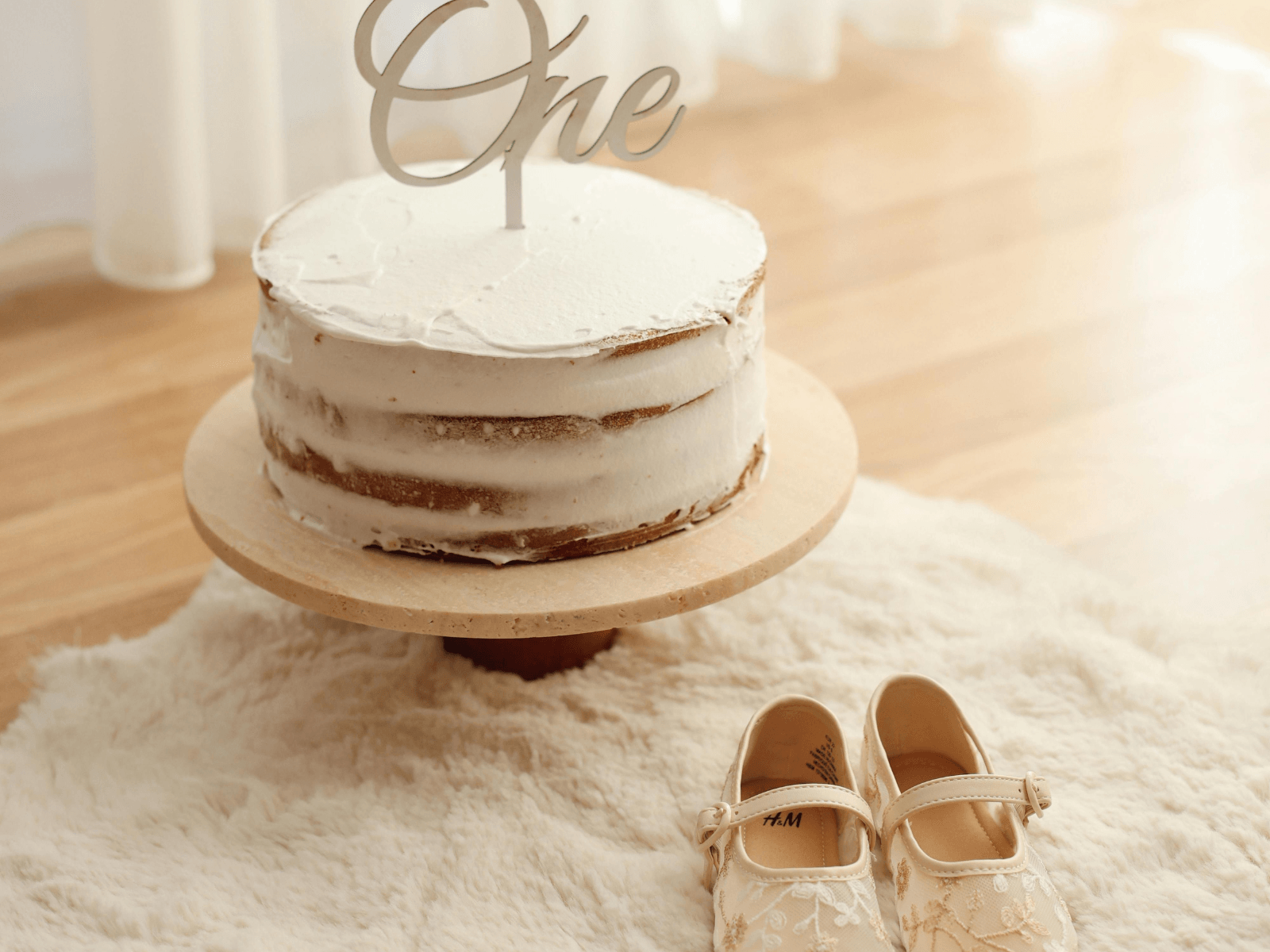 First birthday cake with a “One” topper and baby shoes for 1st birthday wishes.