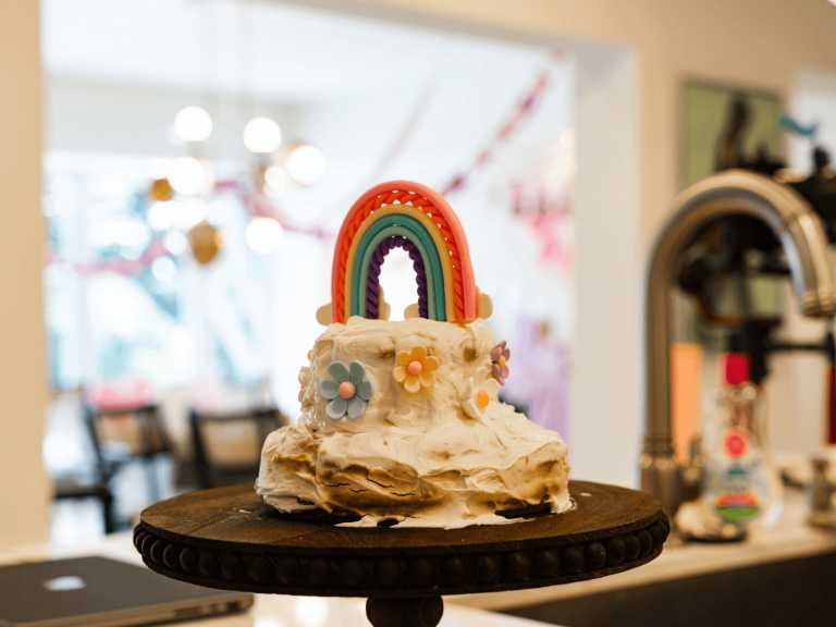 Colorful rainbow and flower decorated cake for a baby’s first birthday celebration.