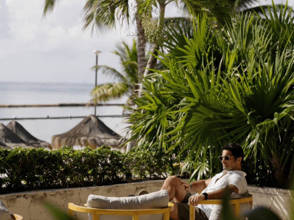 Man wearing sunglasses relaxing in a lounge chair surrounded by tropical palms near the beach at Fairmont Mayakoba.