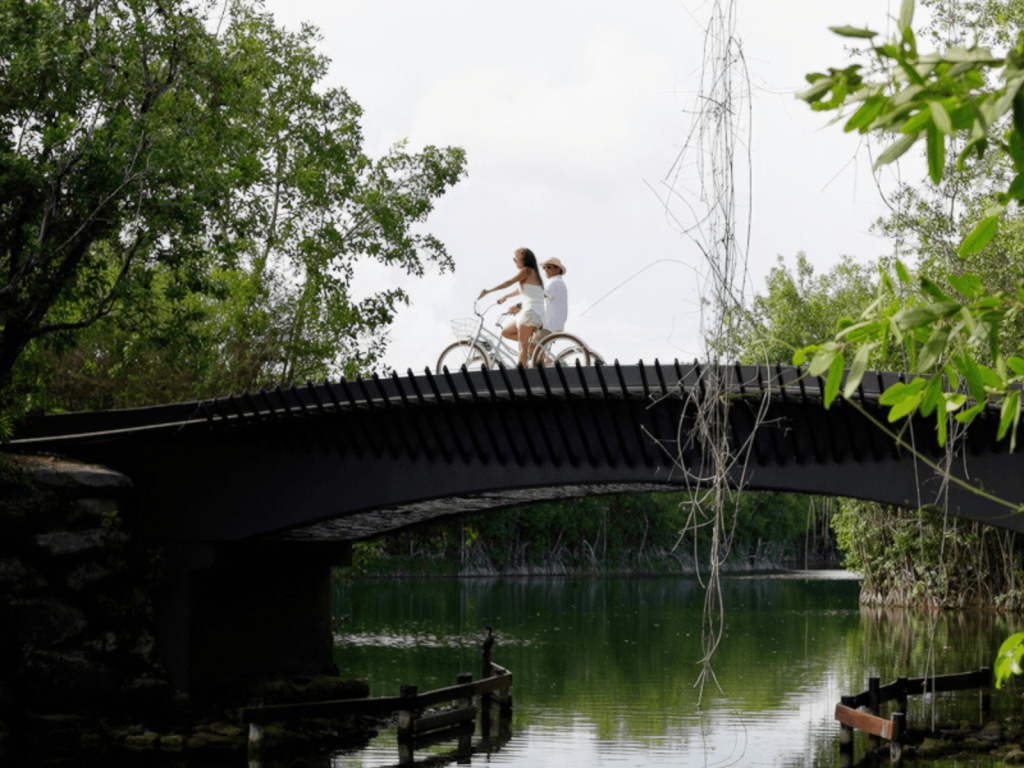 Couple riding complimentary bicycles across a bridge over the mangrove waterways at Fairmont Mayakoba, Mexico.