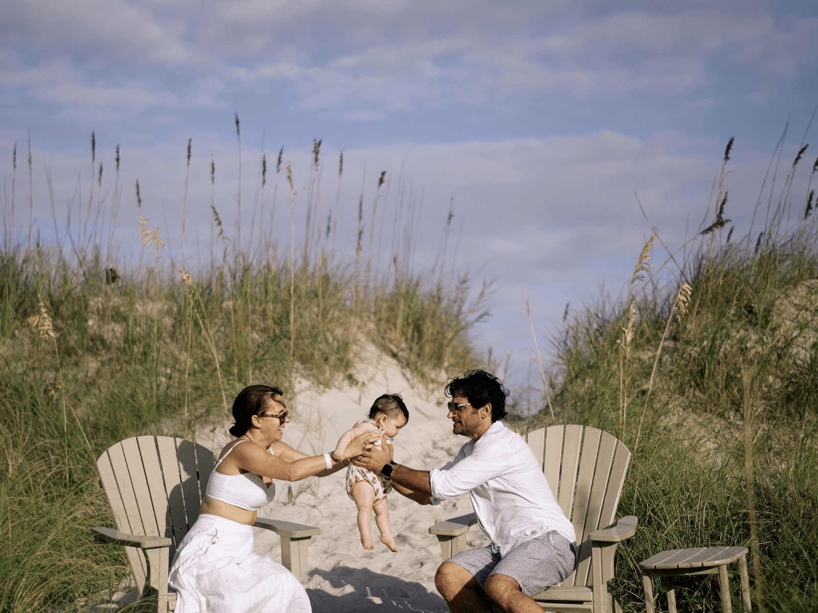 Parents holding their baby between beach chairs in the sand for baby beach essentials.